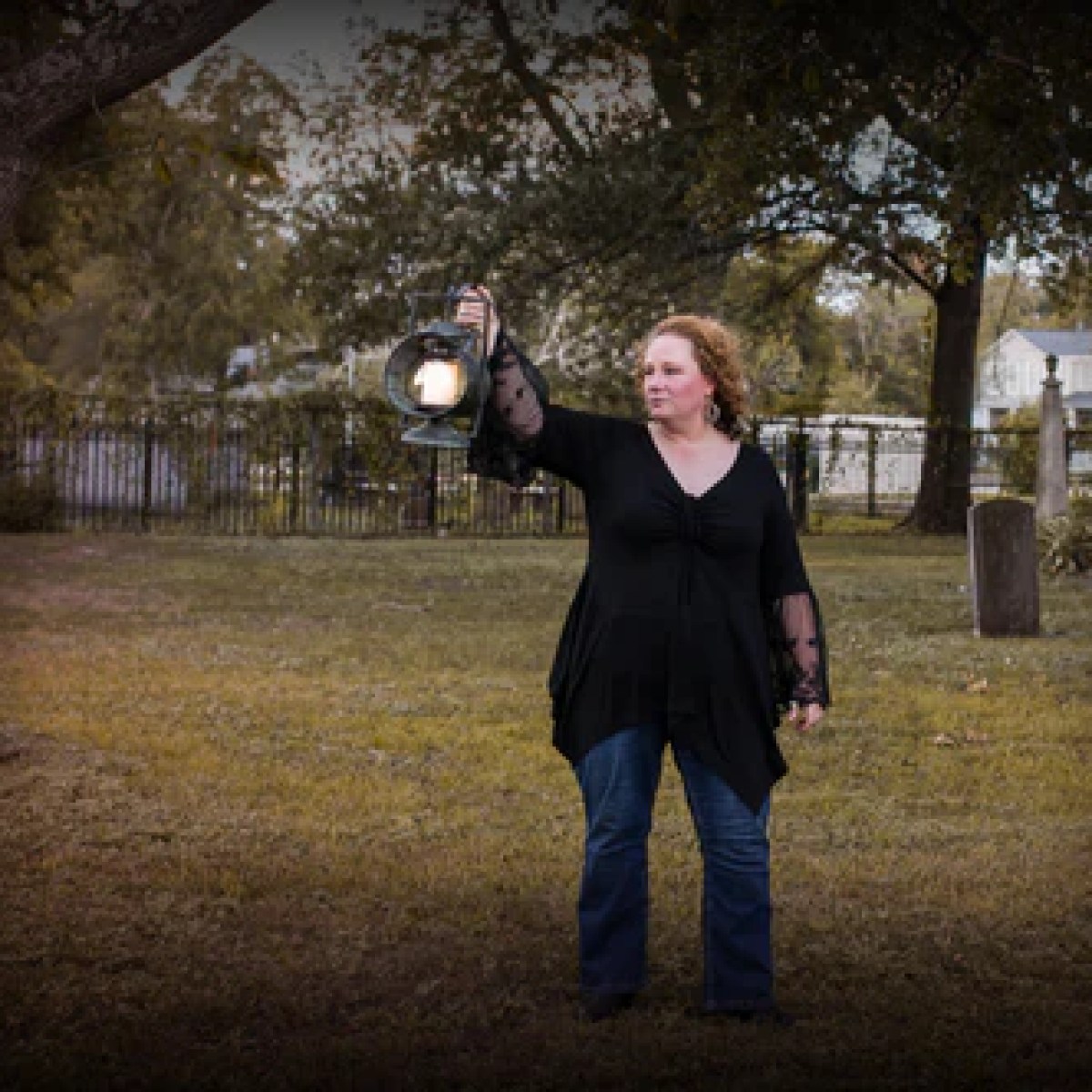 Person holding lantern in a graveyard at dusk.