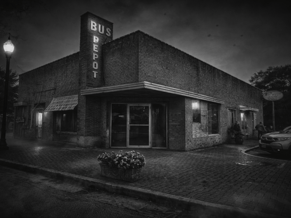 Vintage brick bus depot at night with streetlight and parked car.