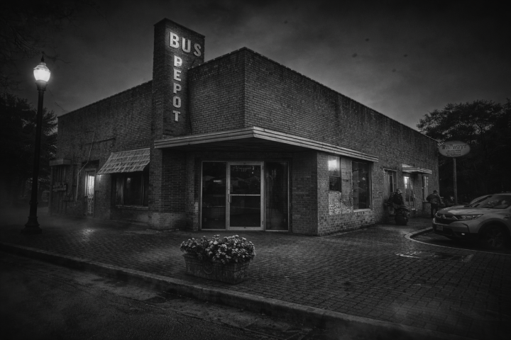 Vintage brick bus depot at night with streetlight and parked car.