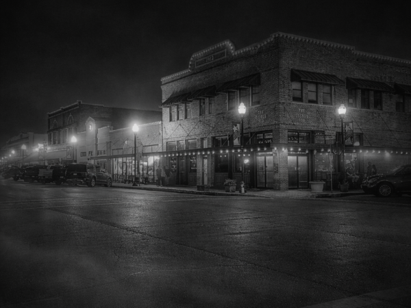 Black and white image of a dimly lit historic street corner at night.