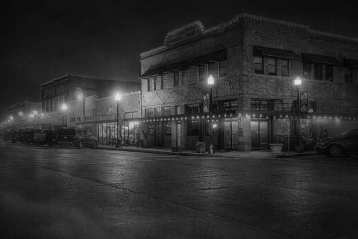 Black and white image of a dimly lit historic street corner at night.