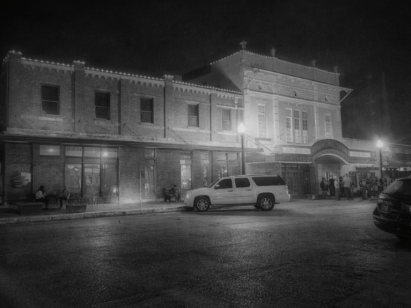 Nighttime view of an illuminated historic brick building with cars parked in front.