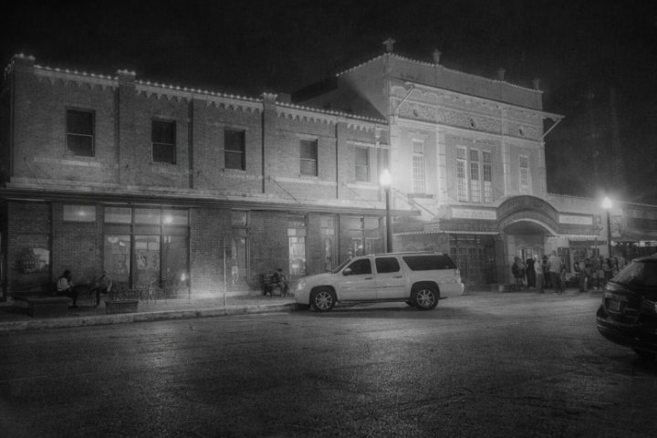 Nighttime view of an illuminated historic brick building with cars parked in front.