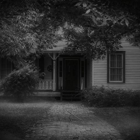 Foggy black and white image of an old house with a porch and overhanging trees.