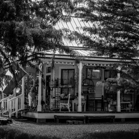 Monochrome photo of a porch with trees, flags, and a person standing.