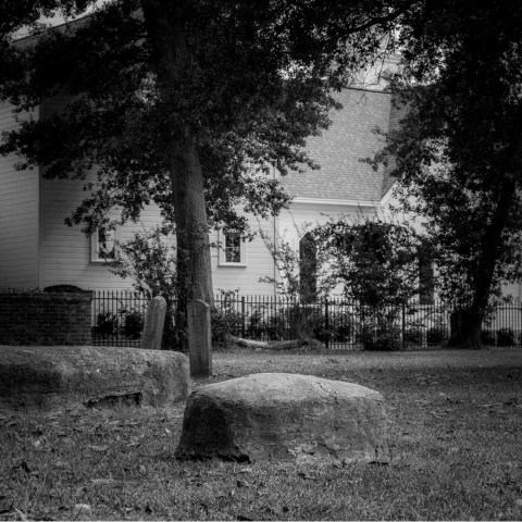 Black and white scene of a grassy yard with stone posts and a house in the background.