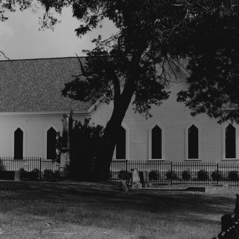 Black and white image of a church with arched windows and trees in the foreground.