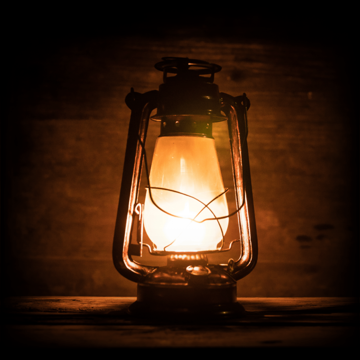 Old-fashioned lantern with warm glow on wooden surface.