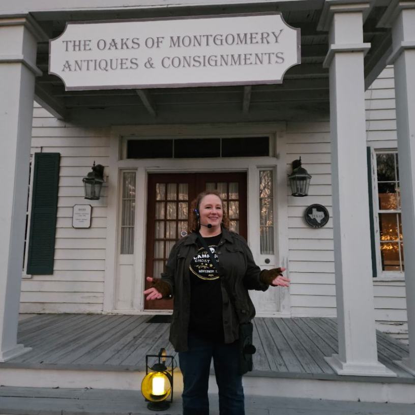 Person standing in front of an antiques store holding a lantern.